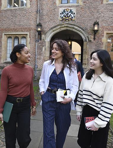Three students chatting whilst walking through First Court
